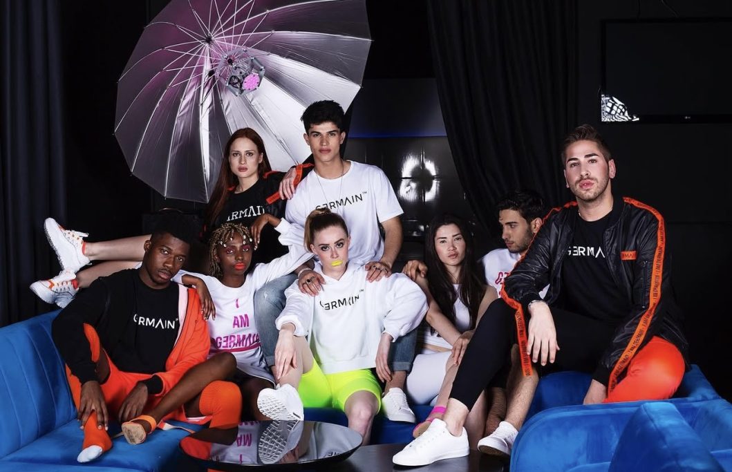 Gruppe junger Menschen in modischer Sportkleidung, lächelnd auf einem blauen Sofa.