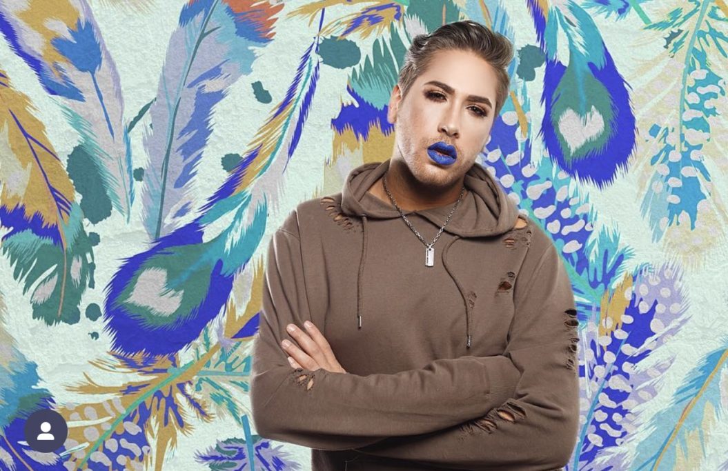 Männliches Model (Joel) mit blauem Lippenstift und brauner Jacke vor buntem, floralem Hintergrund. Congstar Kampagne